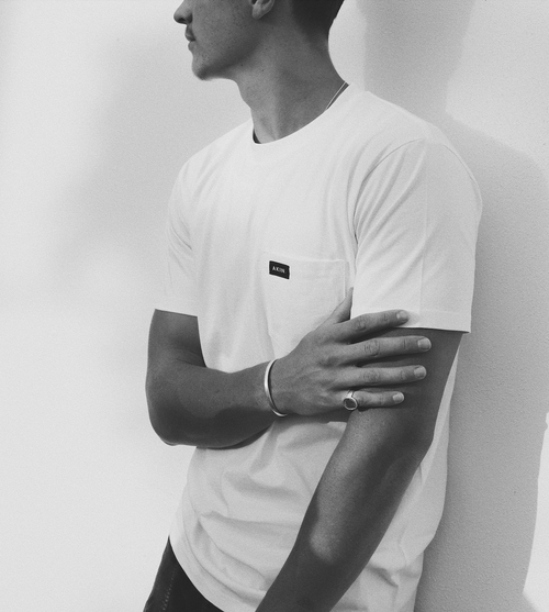 Man in side profile wearing white Akin pocket t-shirt, arms crossed, black and white photo