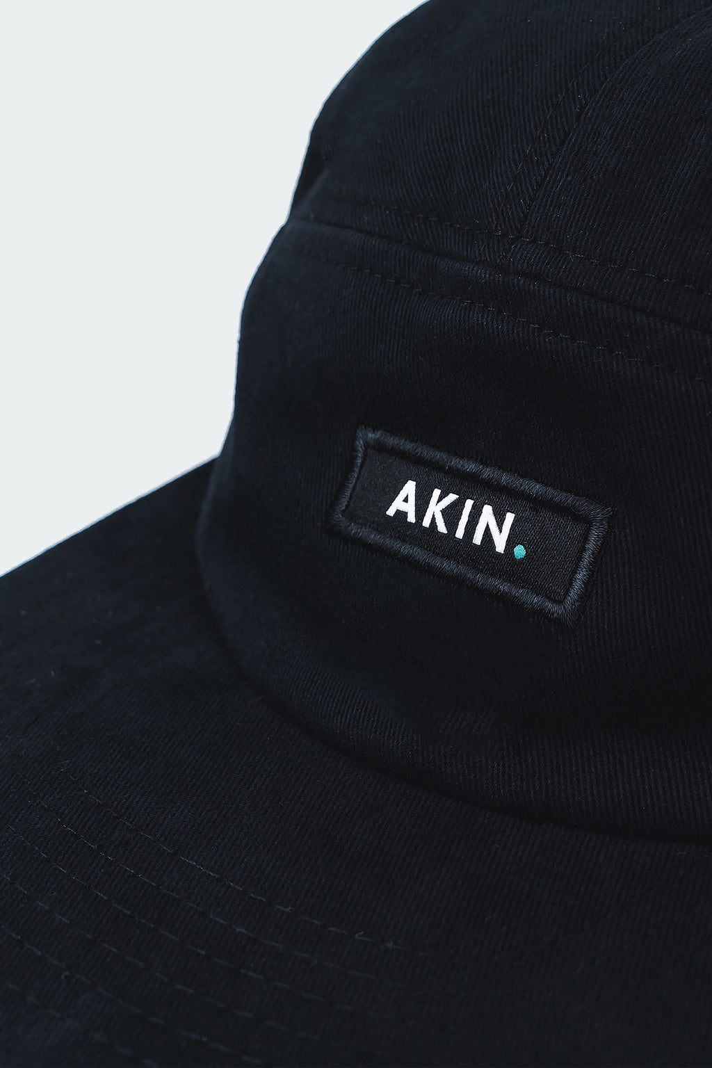 Close-up of white AKIN label on the front panel of the black Akin Five Panel Cap