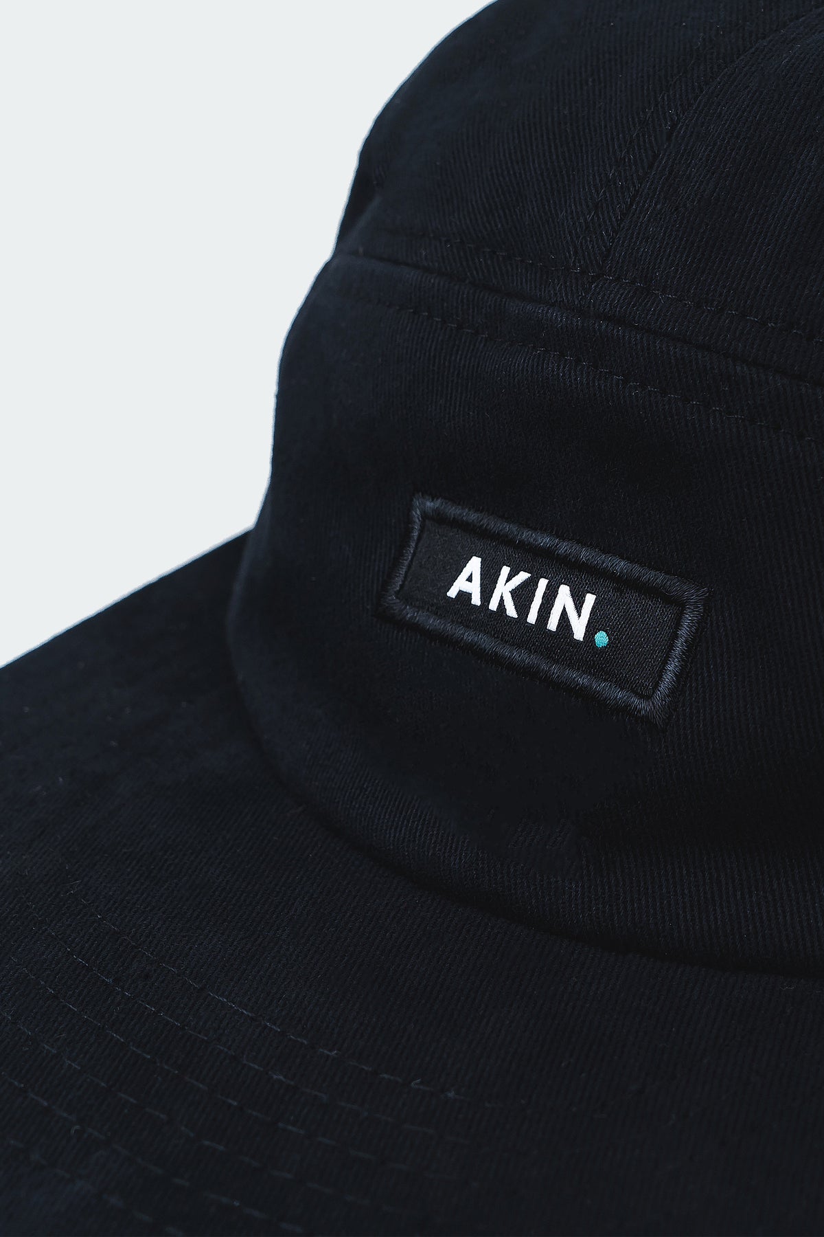 Close-up of white AKIN label on the front panel of the black Akin Five Panel Cap