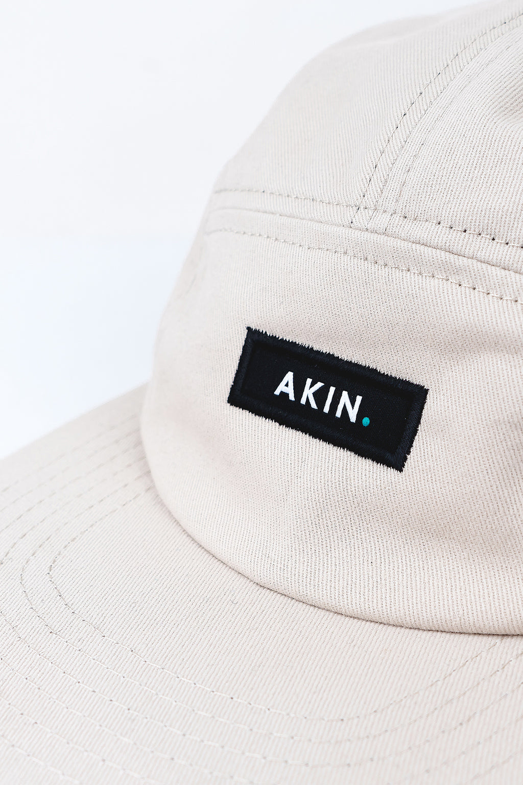 Close-up of black AKIN label on the front panel of the beige Akin Five Panel Cap