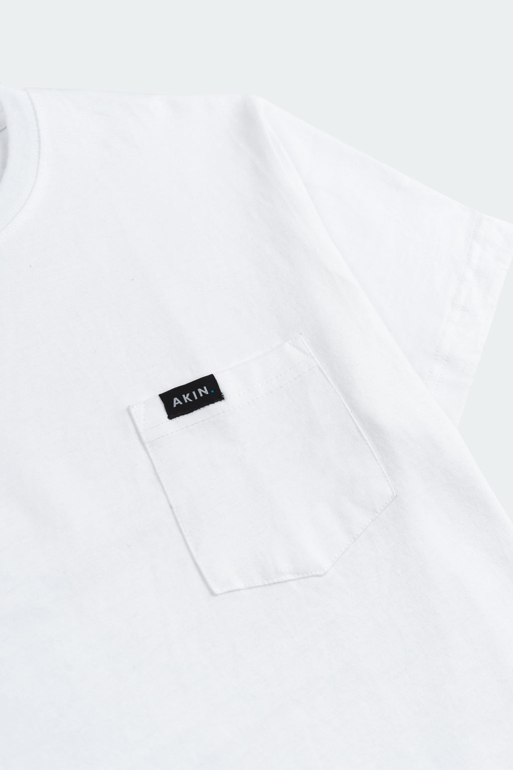 Close-up of white Essential Pocket T-Shirt chest pocket with black Akin label