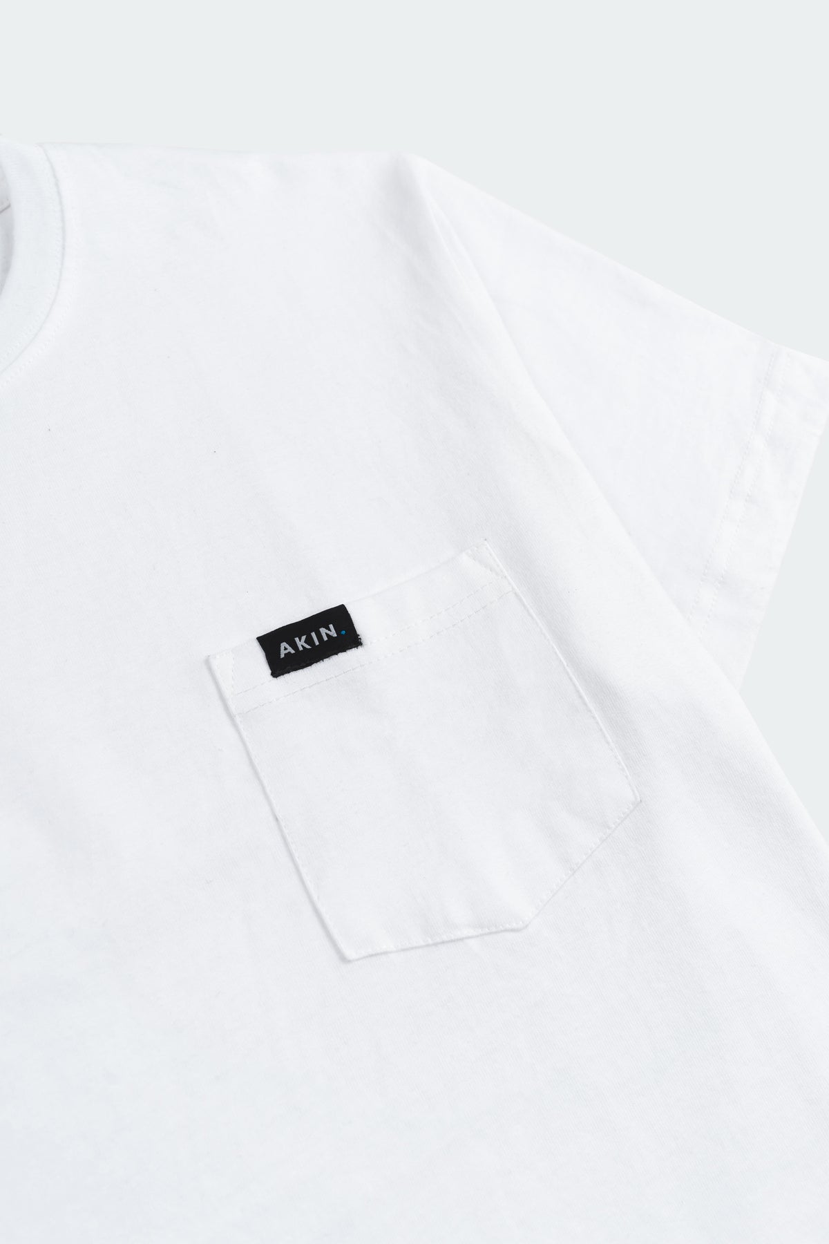Close-up of white Essential Pocket T-Shirt chest pocket with black Akin label