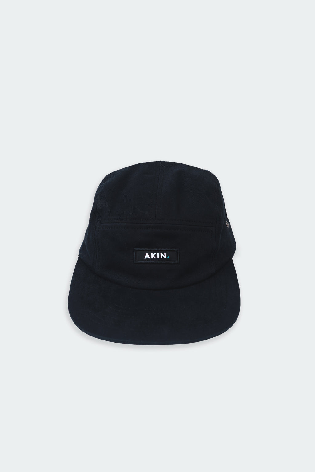 Black Akin Five Panel Cap, front view with white AKIN label, product flat lay