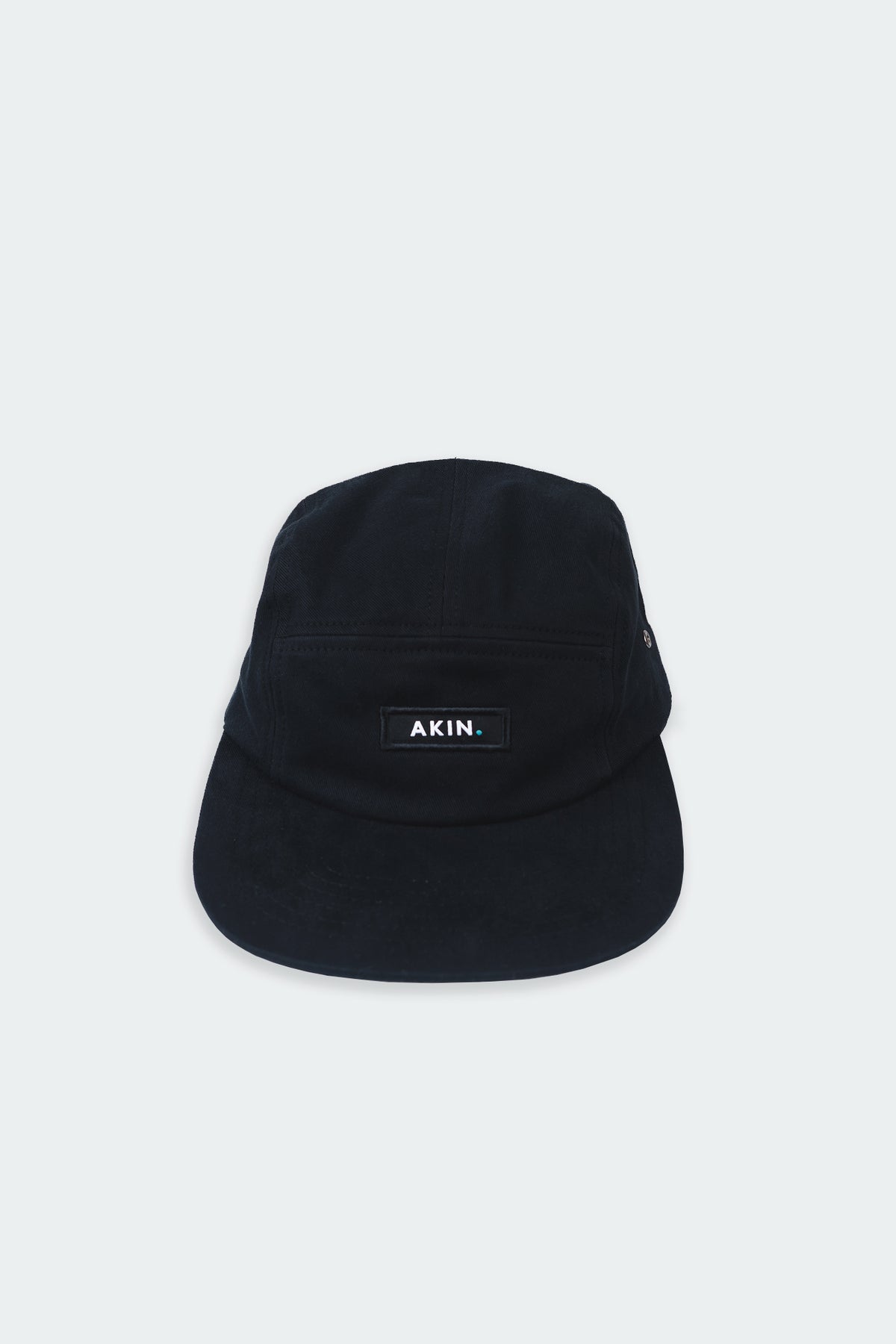 Black Akin Five Panel Cap, front view with white AKIN label, product flat lay