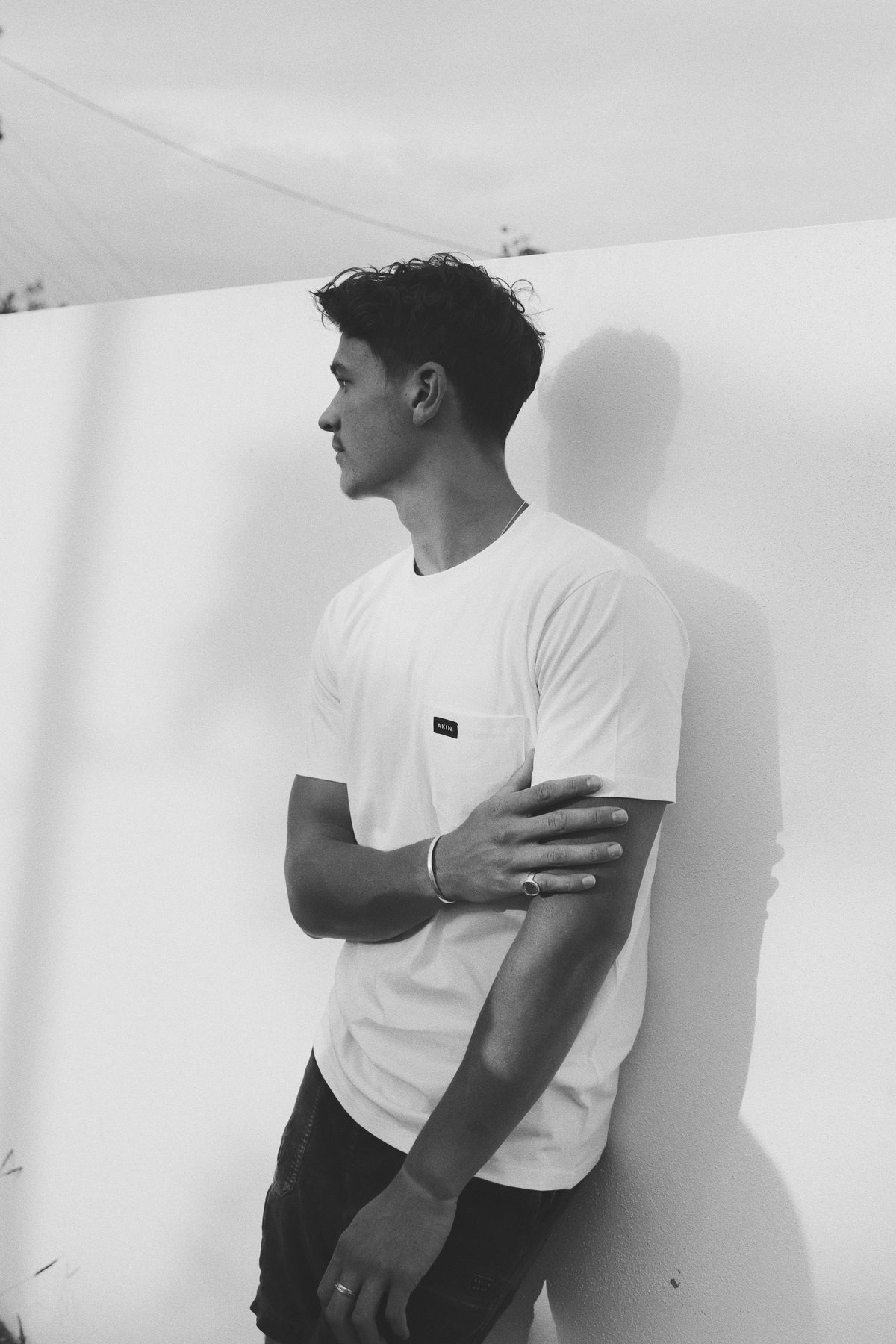 Model wearing white Essential Pocket T-Shirt, side profile against plain wall, black and white photo